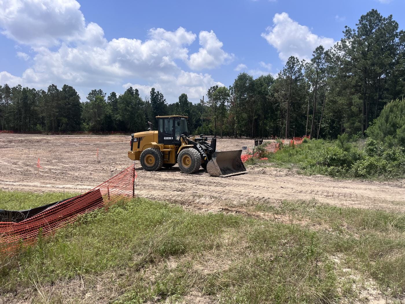 A SANY wheel loader on a cleared site, with silt fence and orange safety fence along the edge.