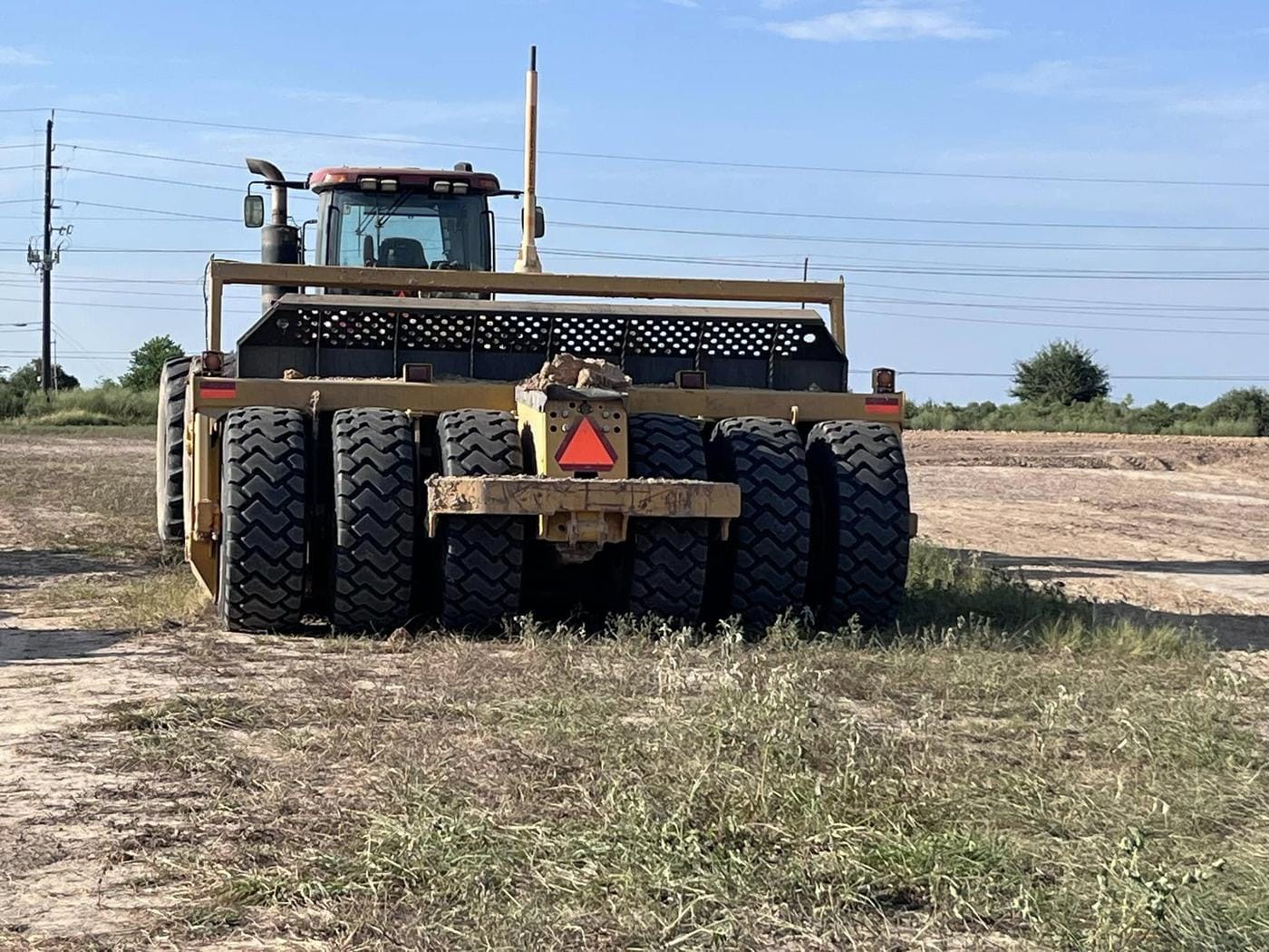 A tractor-pulled rubber-tire roller on a cleared site.